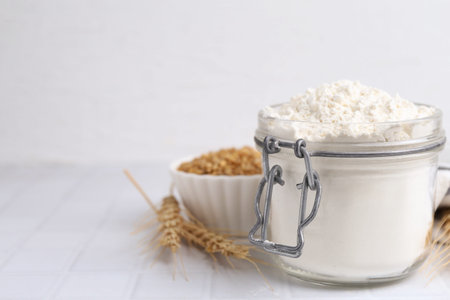 Wheat flour, grain and spikes on white tiled table, closeup. Space for textの写真素材