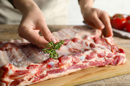 Woman putting thyme onto raw pork ribs at table, closeupの写真素材