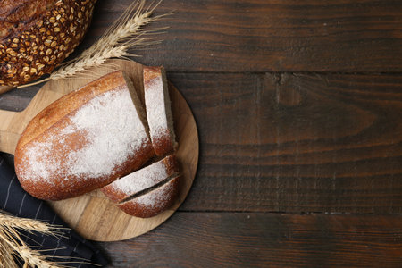 Freshly baked loaves of bread and spikes on wooden table, flat lay. Space for text