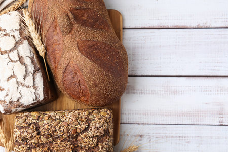 Fresh bread loaves and spikes on white wooden table, flat lay. Space for text