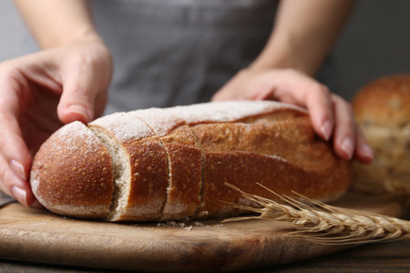 Woman with freshly baked bread at wooden table against grey background, closeupの写真素材