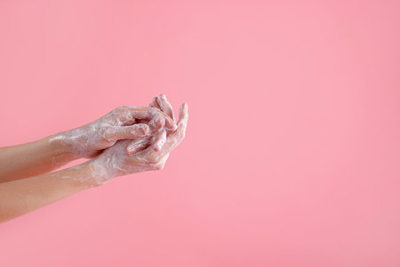 Woman washing hands with soap on light pink background, closeup. Space for text