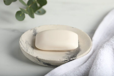 Soap bar, towel and eucalyptus branch on white marble table, closeup
