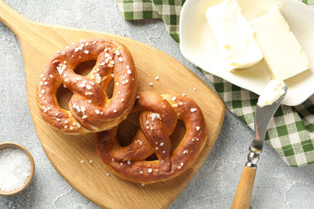 Tasty pretzels with salt and butter on light grey table, flat lay
