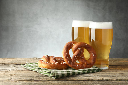 Tasty pretzels and glasses of beer on wooden table against grey background, closeupの写真素材