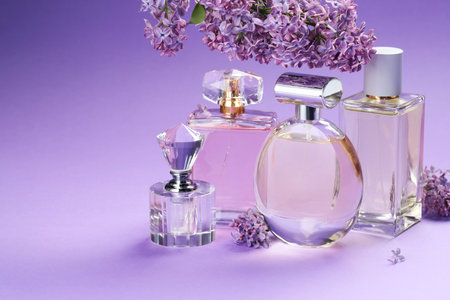 Bottles with perfumes and lilac flowers on purple gradient background, closeup. Space for textの写真素材