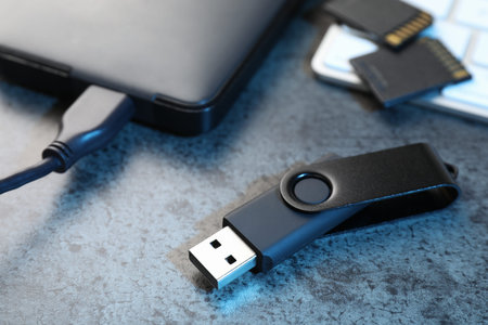 SD memory cards, USB flash drive, hard disk drive with cable and keyboard on dark grey table,...