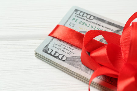 Money bonus. Dollar banknotes with bow on white wooden table, closeup