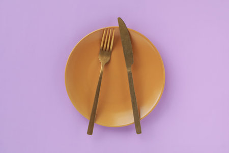 Empty plate and cutlery on violet background, top viewの写真素材