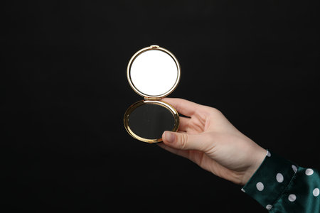 Woman holding open pocket mirror on black background, closeupの写真素材