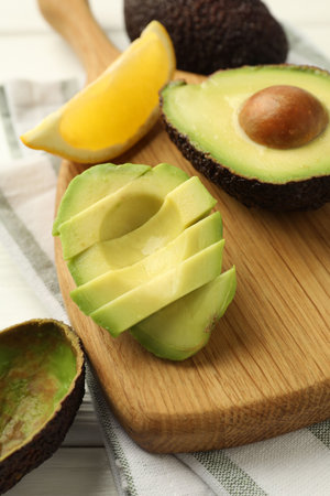 Tasty cut avocados and lemon on white wooden table, closeup