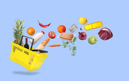 Food products flying into yellow shopping basket on pale blue backgroundの写真素材