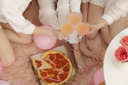 Pajama day. Friends with glasses of alcoholic drink and pizza on faux fur, above viewの写真素材