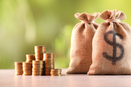 Burlap bags and stacked coins on table against blurred backgroundの写真素材