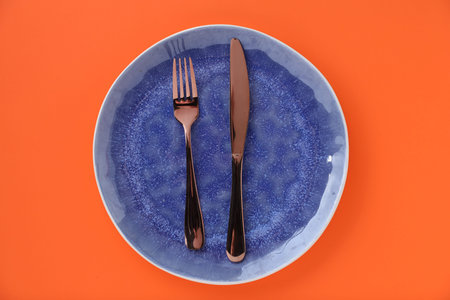 Empty plate and cutlery on orange background, top view