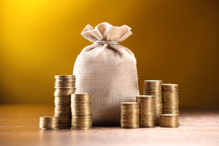 Bag and stacked coins on table against dark yellow gradient backgroundの写真素材