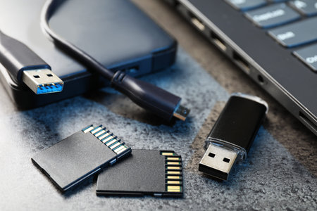 SD memory cards, USB flash drive, hard disk drive with cable and laptop on dark grey table, closeup