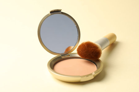 Open face powder with mirror and brush on beige background, closeup