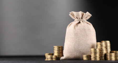 Bag and stacked coins on black table against gray gradient background, space for textの写真素材