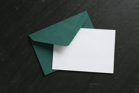 Blank invitation card and envelope on black table, top view. Space for design