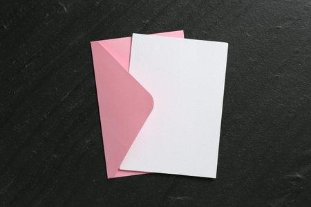 Blank invitation card and envelope on black table, top view. Space for design
