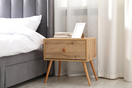 Bedside table with books and frame near bed indoorsの写真素材