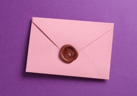 Beautiful invitation envelope with wax seal on purple background, top view
