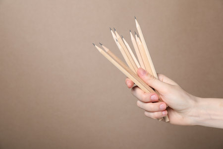 Woman with graphite pencils on beige background, closeup. Space for textの写真素材