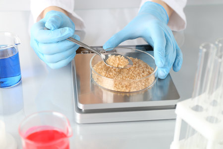 Scientist weighing Petri dish with sample on scales at white mirror table, closeupの写真素材