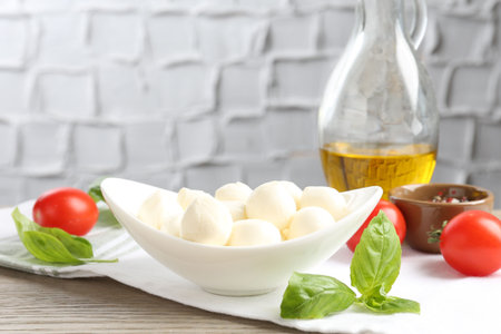 Tasty mozzarella cheese balls, tomatoes, basil, oil and peppercorns on wooden table, closeupの写真素材