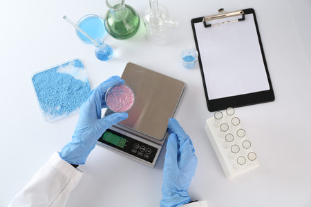 Scientist working with Petri dish of sample and scales at white table, top view
