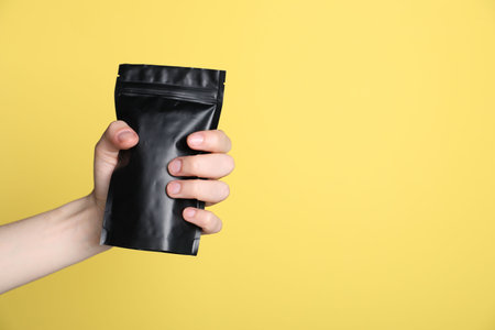 Woman with zipper stand-up pouch on yellow background, closeup. Mockup for designの写真素材