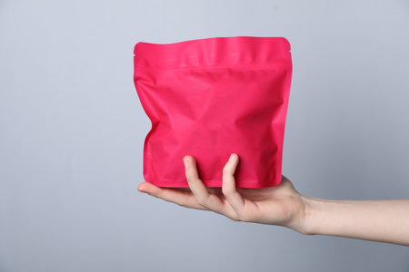 Woman with zipper stand-up pouch on grey background, closeup. Mockup for designの写真素材