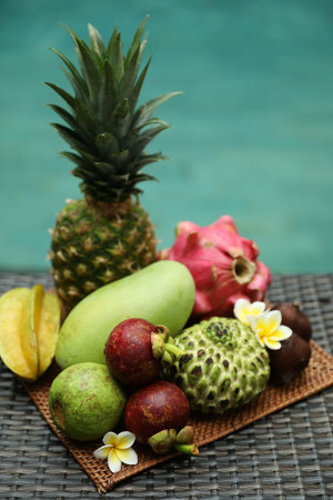 Different tropical fruit on wicker table near swimming poolの写真素材