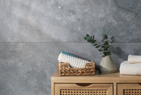 Waffle towels and vase with branches on wooden dresser near grey wall, space for text