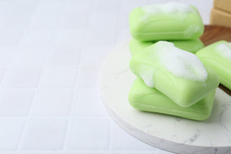 Soap bars with foam on white table, closeup. Space for text
