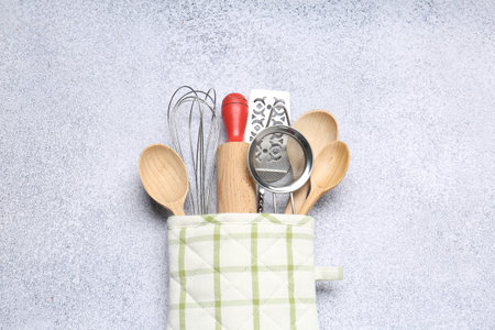 Different kitchen utensils in oven mitten on light table, top view