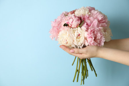 Woman holding bouquet of beautiful peonies on light blue background. Space for textの写真素材