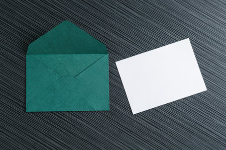 Blank invitation card and envelope on black textured table, flat lay. Space for designの写真素材