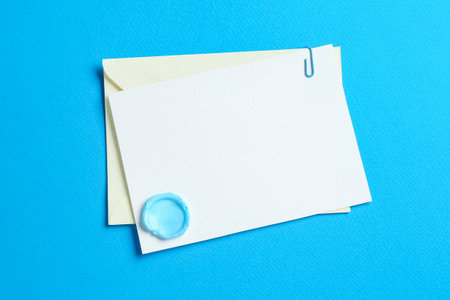 Blank invitation card with wax seal and envelope on light blue background, top view. Space for designの写真素材