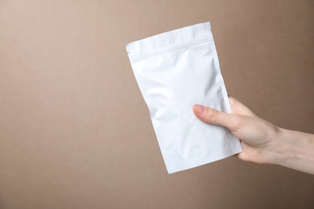 Woman with zipper stand-up pouch on beige background, closeup. Mockup for designの写真素材