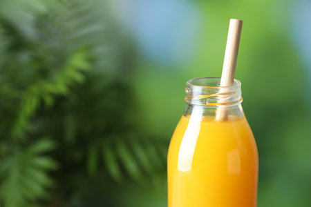 Tasty mango juice in glass bottle on blurred background, closeup. Space for textの写真素材