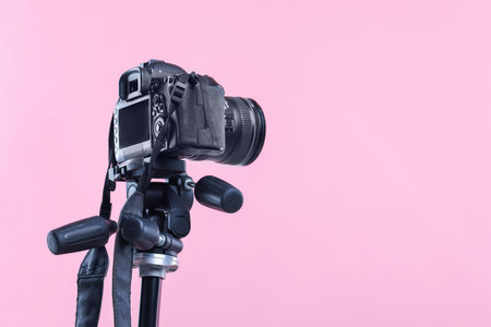 Modern professional video camera on pink background, low angle view. Space for text