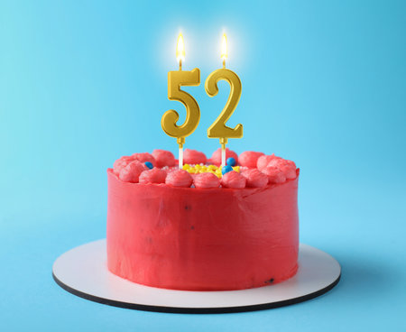 Yummy cake with burning number shaped candles on light blue background. 52th birthday or other special occasionの写真素材