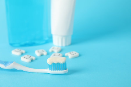 Different oral care products and teeth figures on light blue background, closeup