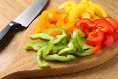 Slices of fresh colorful bell peppers and knife on wooden table, closeupの写真素材
