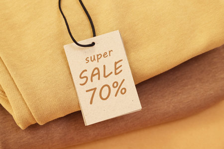 Sale tag and clothes on pale brown background, closeup