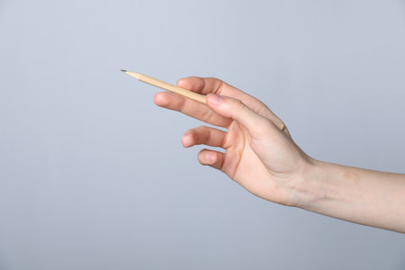 Woman with graphite pencil on grey background, closeup. Space for textの写真素材