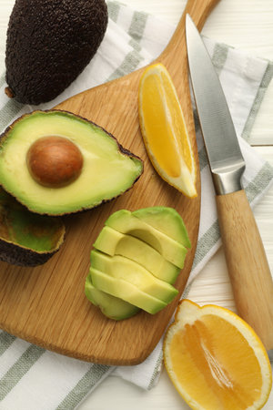 Tasty cut avocados, lemon and knife on white wooden table, flat lay