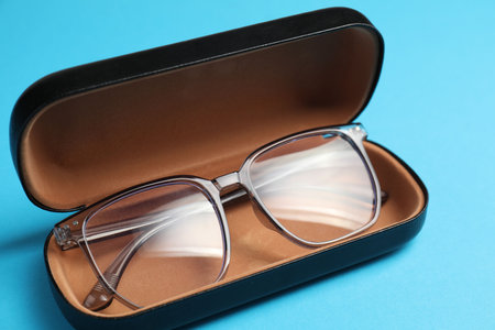 Case with stylish glasses on light blue background, closeup